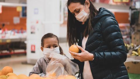 A mother and daughter wear masks while shopping for groceries.
