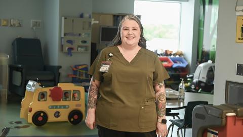 A woman stands in front of a children's play station, with a variety of toys in the background. 