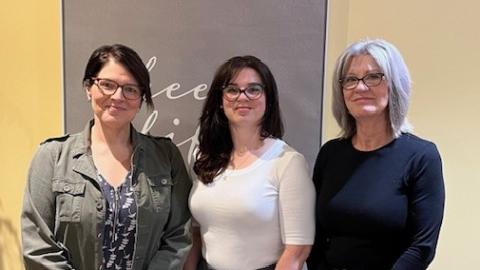 Three women stand side-by-side in front of a wall