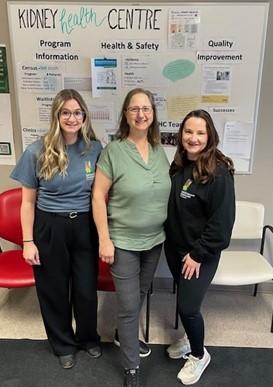 Three health-care professionals standing together in front of a white board that reads “Kidney Health Centre”
