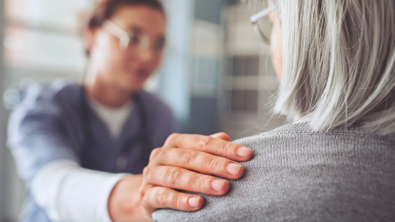 Two women are facing each other and one woman has her hand on the other woman’s shoulder.