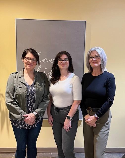Three women stand side-by-side in front of a wall