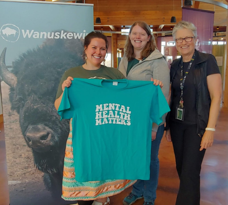 Three women stand together showing a shirt that displays the text Mental Health Matters